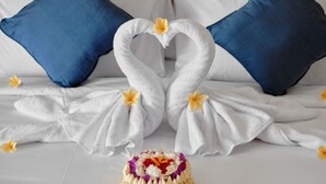 Ein Bett mit weißen und blauen Kissen, ein weißes Handtuch in Herzform drapiert und eine kleine Blumenkomposition auf dem Bett.