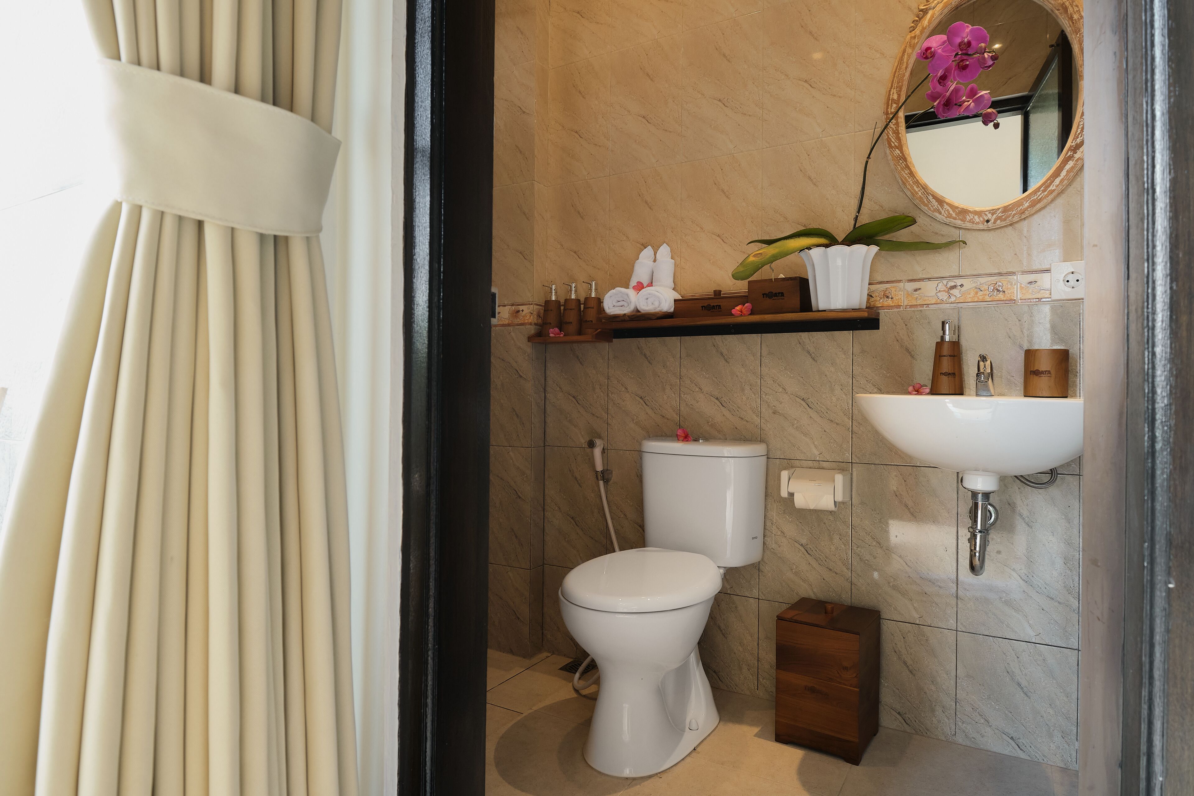 A bathroom with a toilet, sink, and shower. There is a shelf with toiletries and a potted plant.