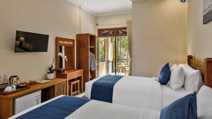 Ein Hotelzimmer mit zwei Betten, einem Schreibtisch, einem Fernseher und einem Balkon mit Blick auf Grünflächen.