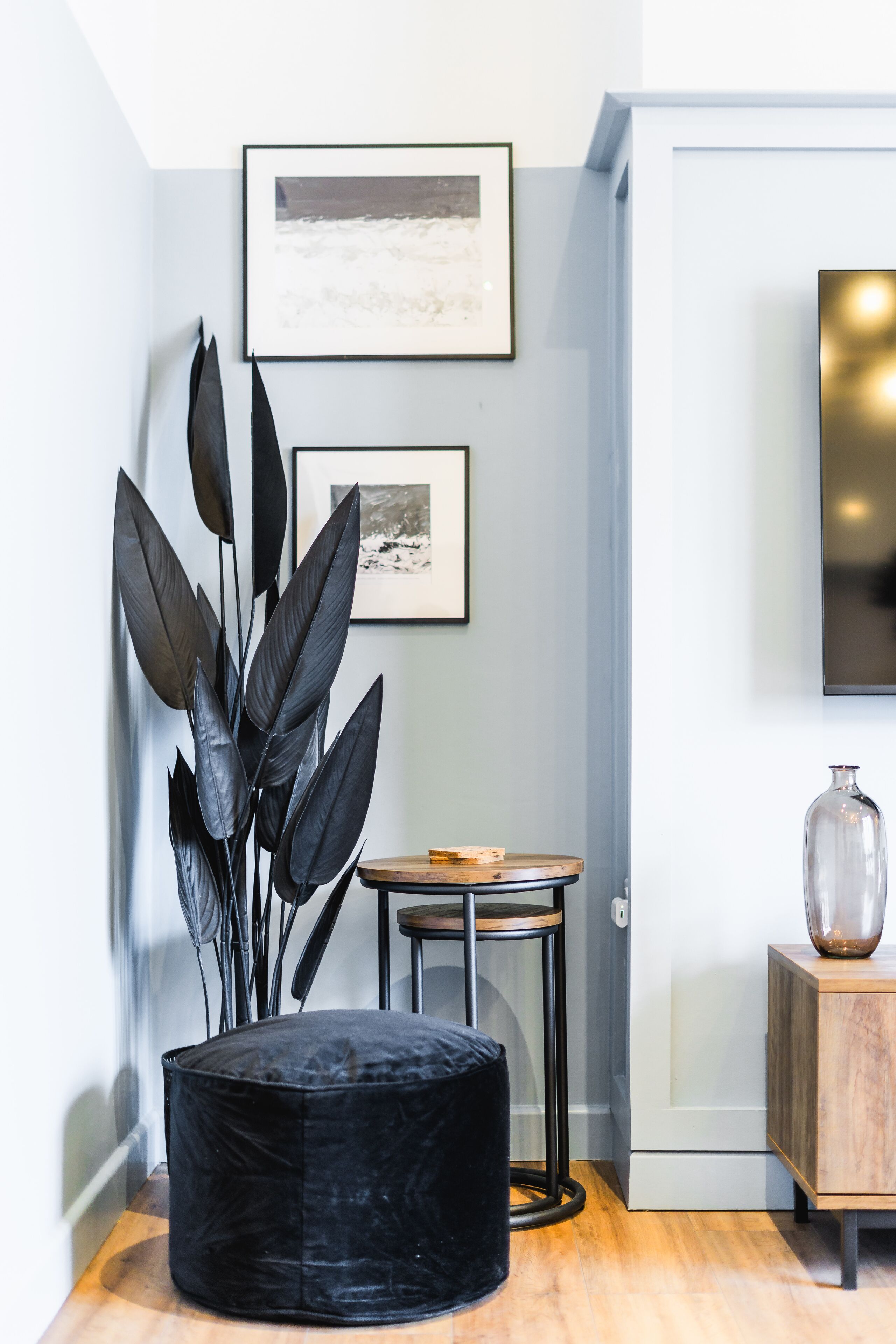 Une pièce comprenant un pouf noir, une petite table ronde et un meuble sur lequel est posé un vase.