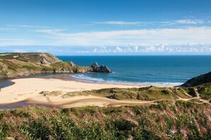 A coastal landscape with a sandy beach, rocky outcrops, and a clear view of the ocean. - Croeso i Faircroft 5 star self-catering for 2 people with sea views in Rhossili. (Swansea)