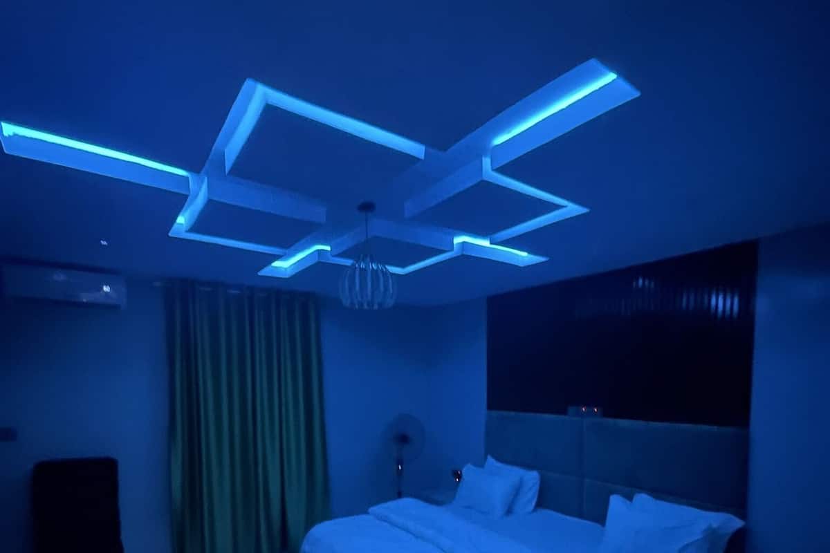 A modern bedroom with a geometric ceiling design, a large bed, and a green curtain.