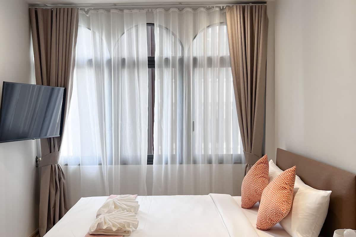 Un lit bien fait, avec des oreillers et une couverture, une table de chevet avec une lampe et un téléviseur fixé au mur.