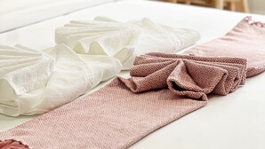 A neatly made bed with white and patterned towels, a wooden desk, and a chair in a hotel room.