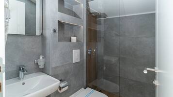 Un baño moderno con ducha de vidrio, lavamanos blanco y un inodoro con etiqueta visible.