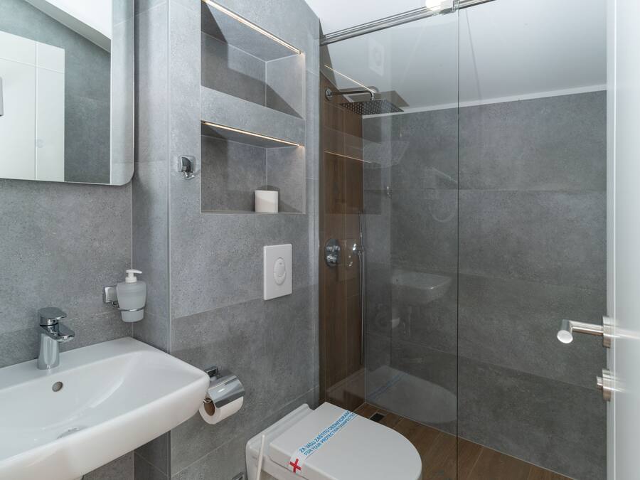 Un baño moderno con ducha de vidrio, lavamanos blanco y un inodoro con etiqueta visible.