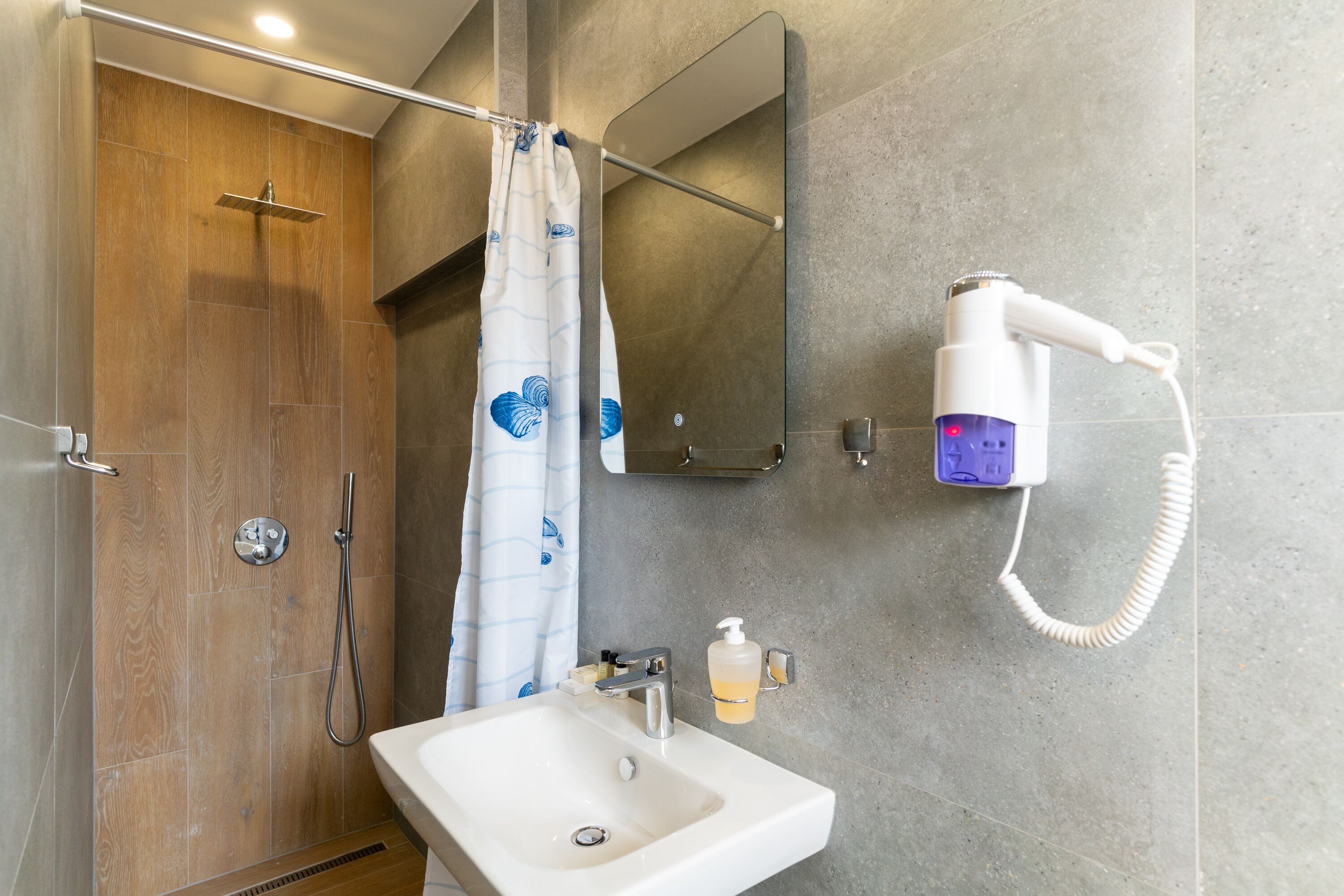 Un baño con ducha, lavamanos, espejo y secador de pelo.