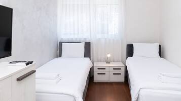 Une chambre d’hôtel avec deux lits simples, une table de chevet avec une lampe, un téléviseur sur le côté gauche et un plancher en bois.