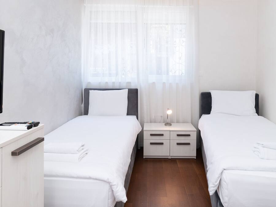 Une chambre d’hôtel avec deux lits simples, une table de chevet avec une lampe, un téléviseur sur le côté gauche et un plancher en bois.