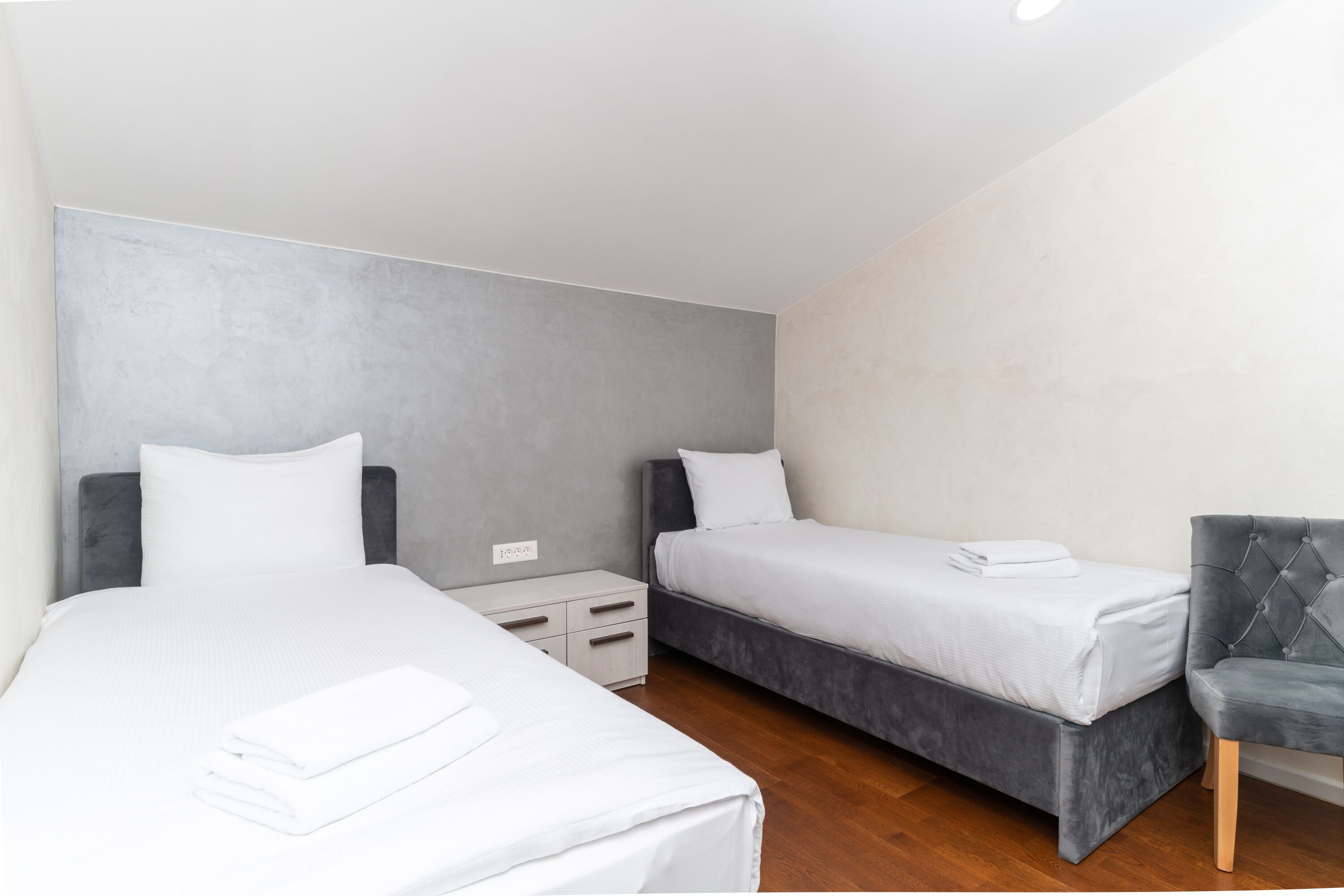 Une chambre d’hôtel avec deux lits, une table de chevet, une chaise et une prise électrique fixée au mur.
