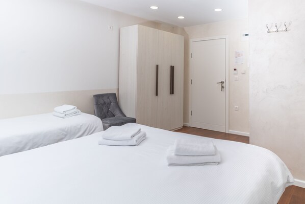 Una habitación de hotel con dos camas individuales, un sillón gris, un armario y una puerta.