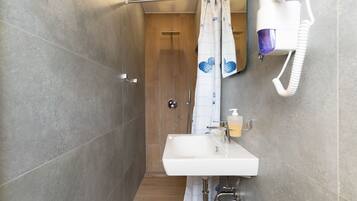 A bathroom with a shower, a sink with a soap dispenser, and a hairdryer mounted on the wall.