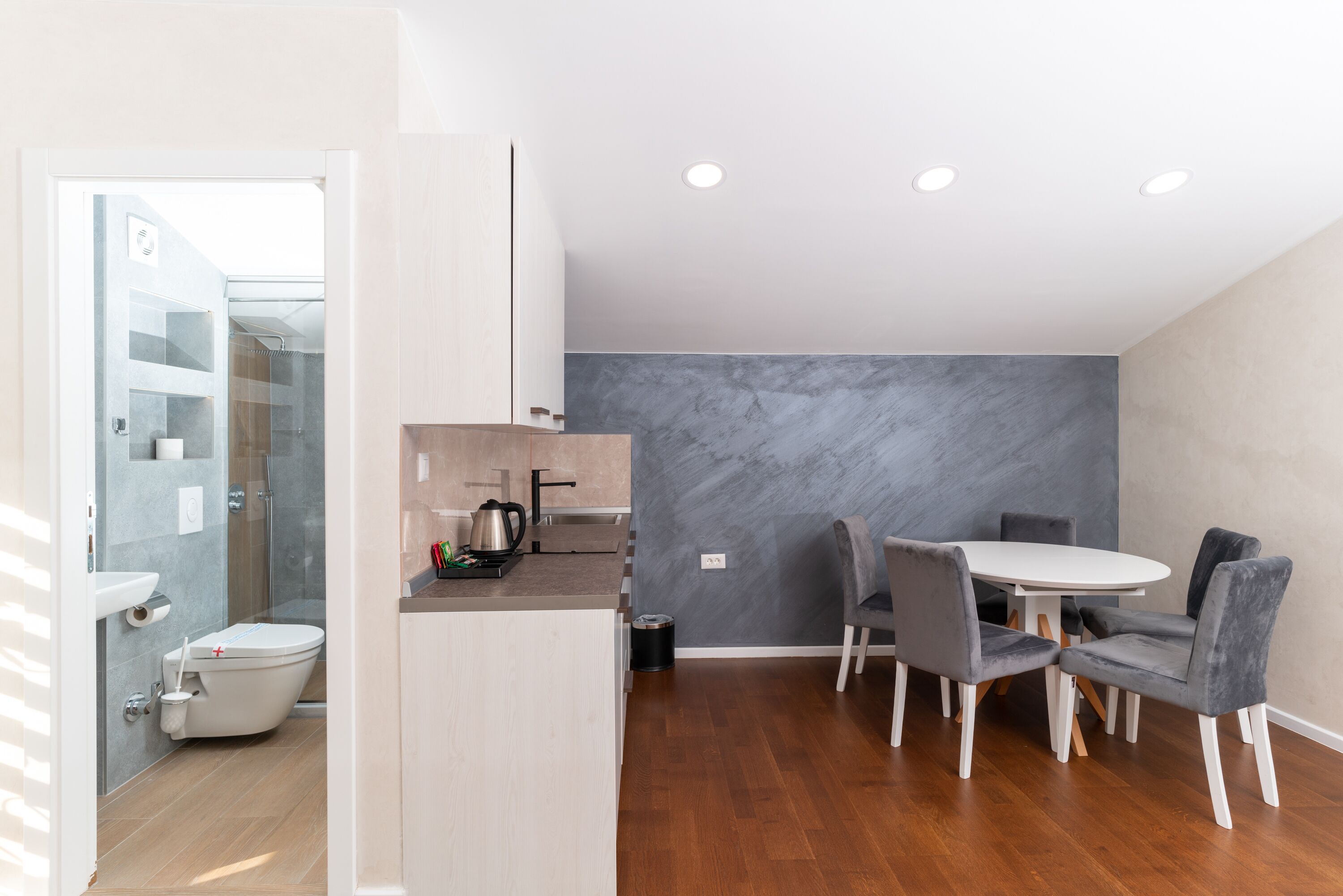 A modern kitchen with a built-in oven, a sink, and a coffee maker. There is a dining area with a round table and four chairs.