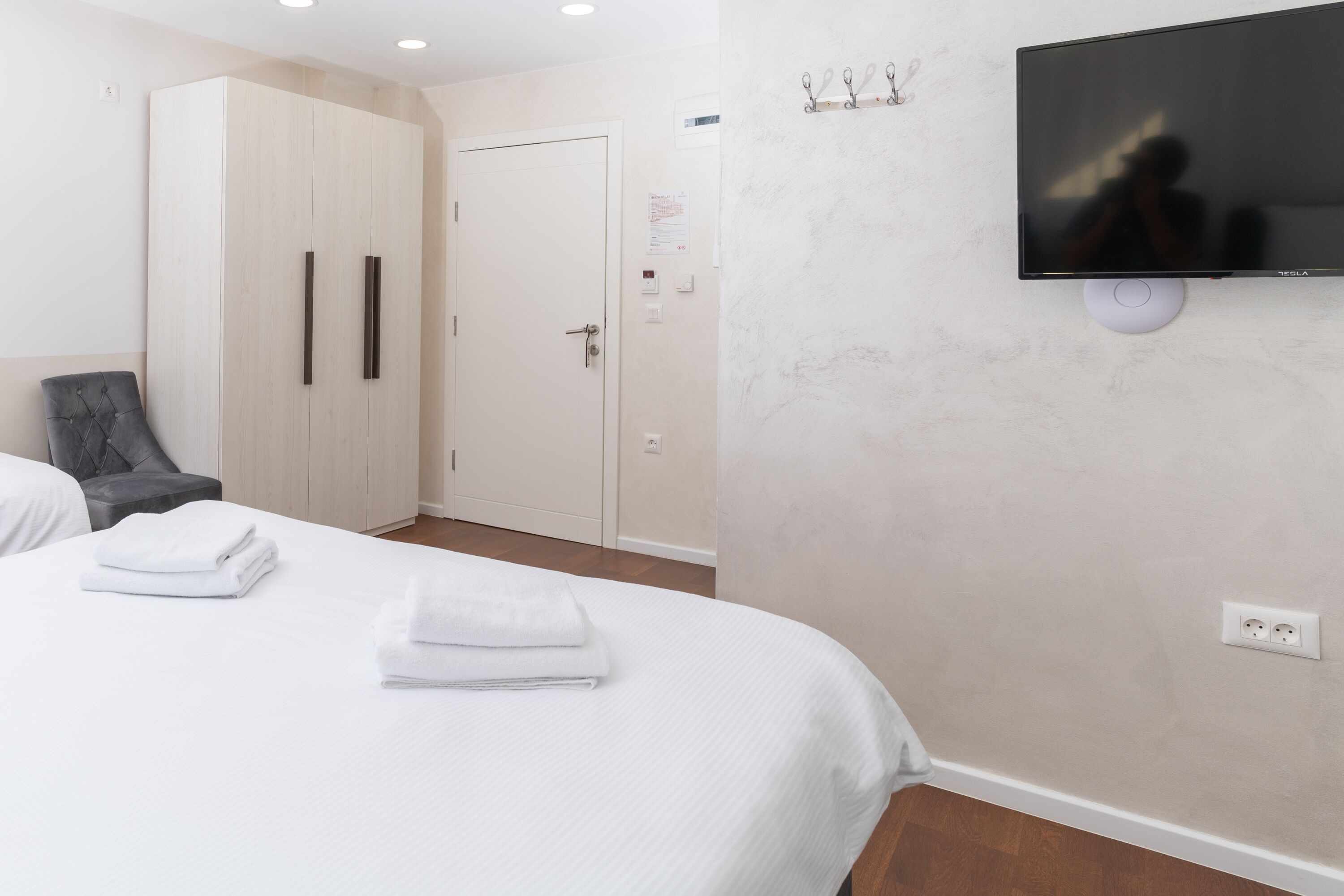 A hotel room with a bed, a wardrobe, a TV mounted on the wall, and a chair.