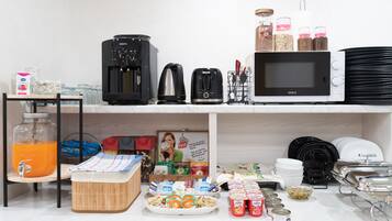 A kitchen area with a coffee maker, kettle, microwave, and various food items on the counter.