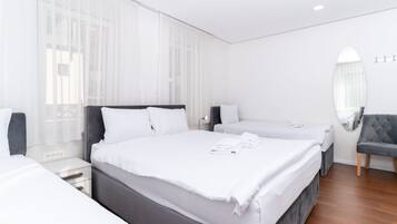 A hotel room with two beds, a large mirror, and a grey armchair.