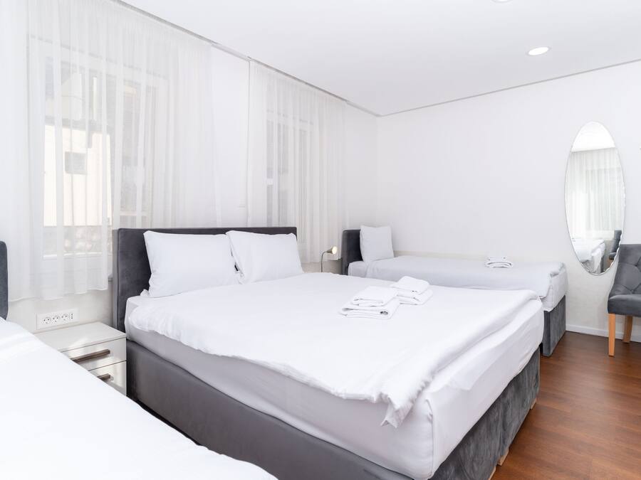 A hotel room with two beds, a large mirror, and a grey armchair.