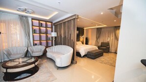 A modern hotel room with a curved sofa, a round coffee table, a bed, and a seating area with two armchairs. - Meethaq Hotels Jabi (Abuja)