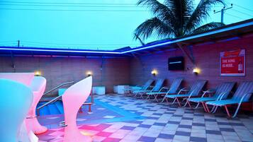 Zona de piscina con sillones de descanso, piso a cuadros y un letrero de Budweiser.