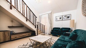 A living room with a staircase, a green sofa, a coffee table, and a patterned rug. - Meethaq Hotels Jabi (Abuja)