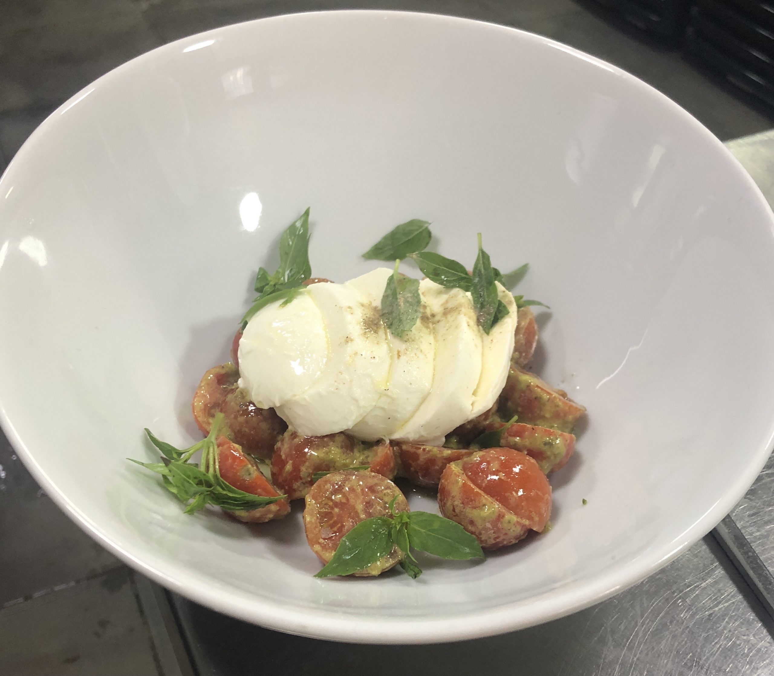 Un bol blanc contenant un plat composé d’une cuillère de crème blanche, de feuilles vertes et de morceaux de tomates.