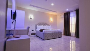 A modern hotel room with a large bed, bedside tables, a desk, and a large window with curtains. - HABAB GRAND RESORT (Abuja)