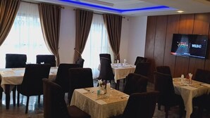 A hotel dining area with multiple tables and chairs, a television screen displaying 'Wild Africa Fund', and a large window with curtains. - HABAB GRAND RESORT (Abuja)