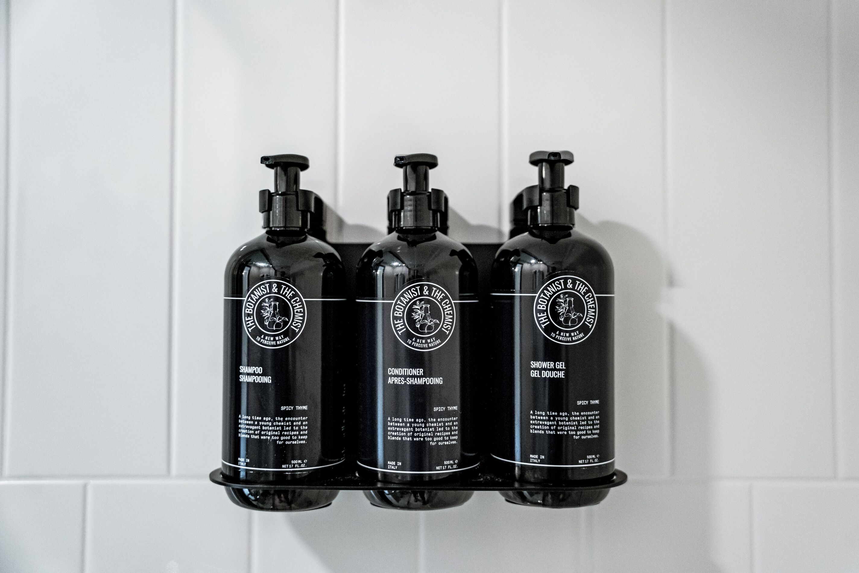 Three black bottles of The Botanist & The Chemist products on a white tiled wall.