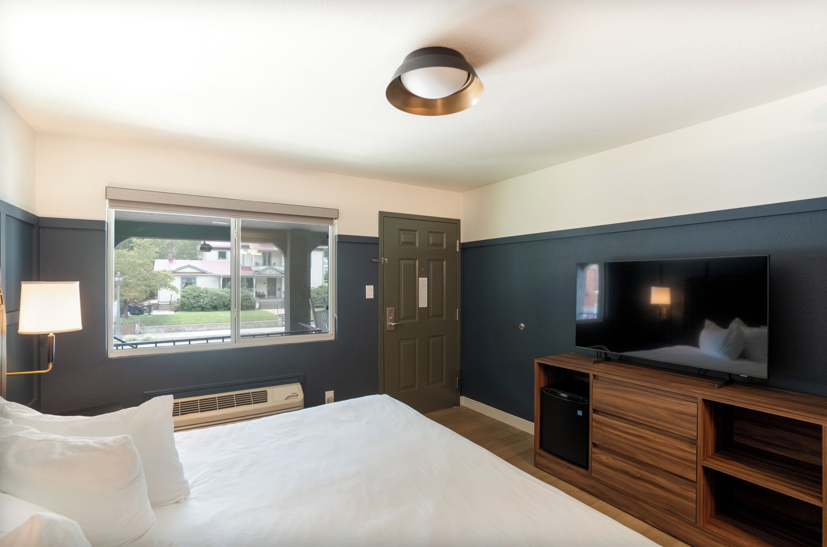 A hotel room with a bed, a TV, a window, and a door.