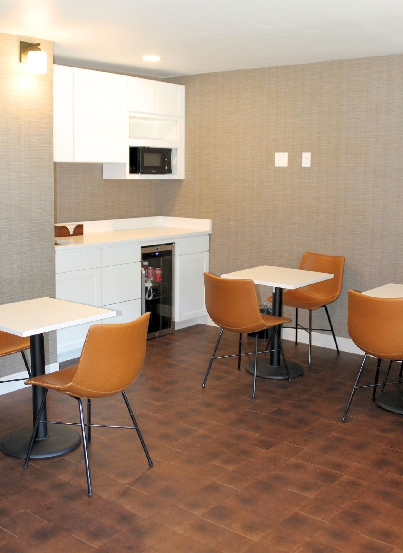 A modern kitchen with white cabinets, a microwave, and a dishwasher. There are four orange chairs around a table.