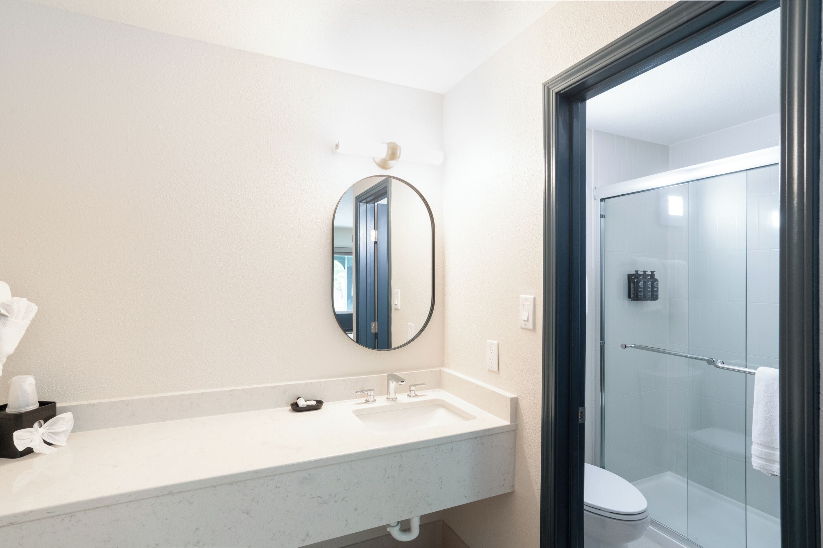 Une salle de bain avec un lavabo blanc, un miroir rond et une douche à parois de verre.