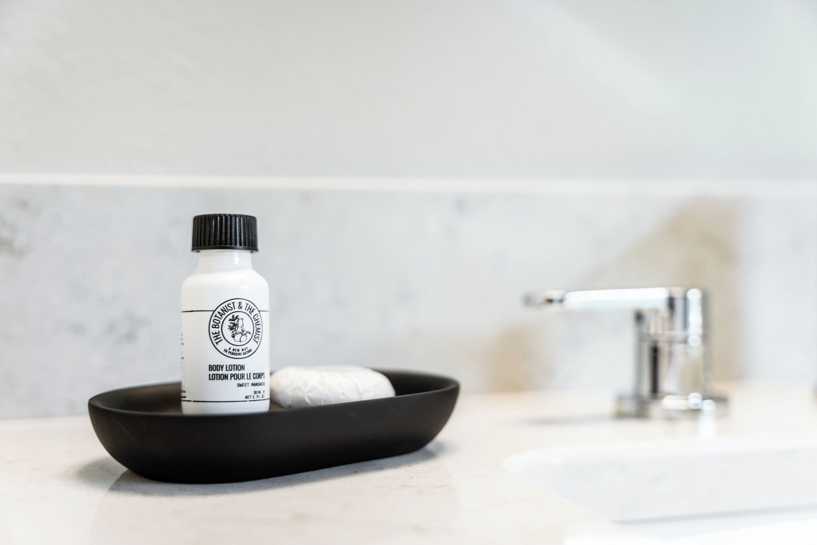 Ein Badezimmer mit einer schwarzen Seifenschale, die eine Seife und eine Flasche Körperlotion auf einer weißen Ablagefläche enthält.