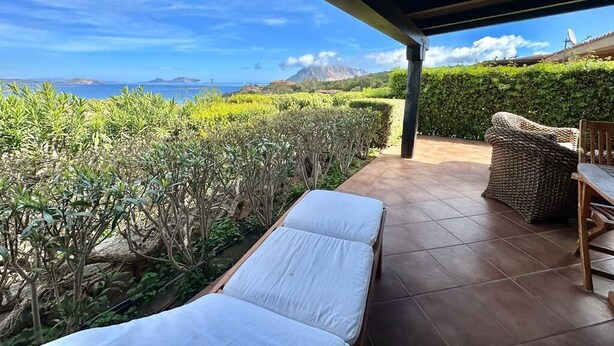 Un espace extérieur abrité, aménagé avec des sièges, offrant une vue sur la mer, comprenant un fauteuil et une table.