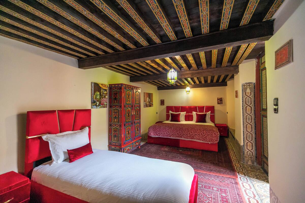 A hotel room with a large bed, a red headboard, a wooden ceiling, and a patterned carpet.