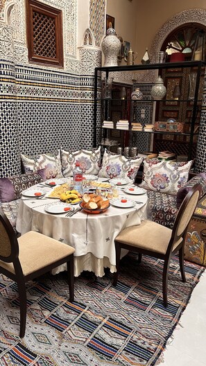 A dining area with a round table set for a meal, surrounded by patterned cushions and a decorative rug. - riad dar hadia fes (Fes)