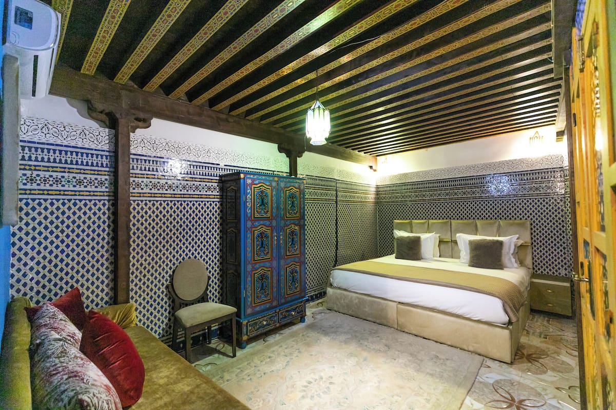 A traditional Moroccan room with a bed, a wooden cabinet, and patterned walls.