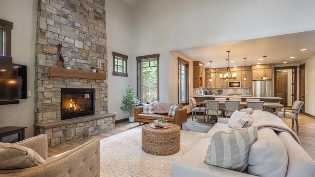 A spacious living room with a stone fireplace, a dining area, and a kitchen with pendant lighting.