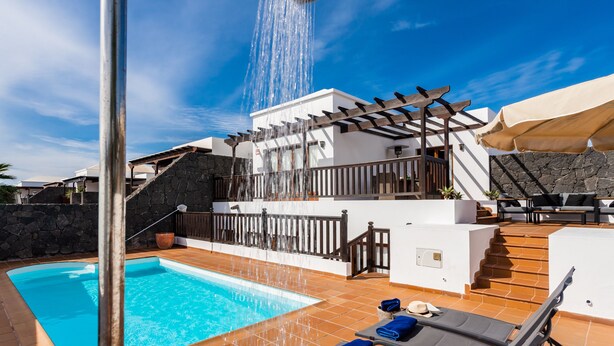 A swimming pool with a waterfall feature, outdoor seating, and a stone wall.