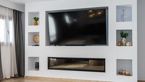 A modern living room with a large flat-screen TV mounted on a white wall, surrounded by shelves with decorative items.