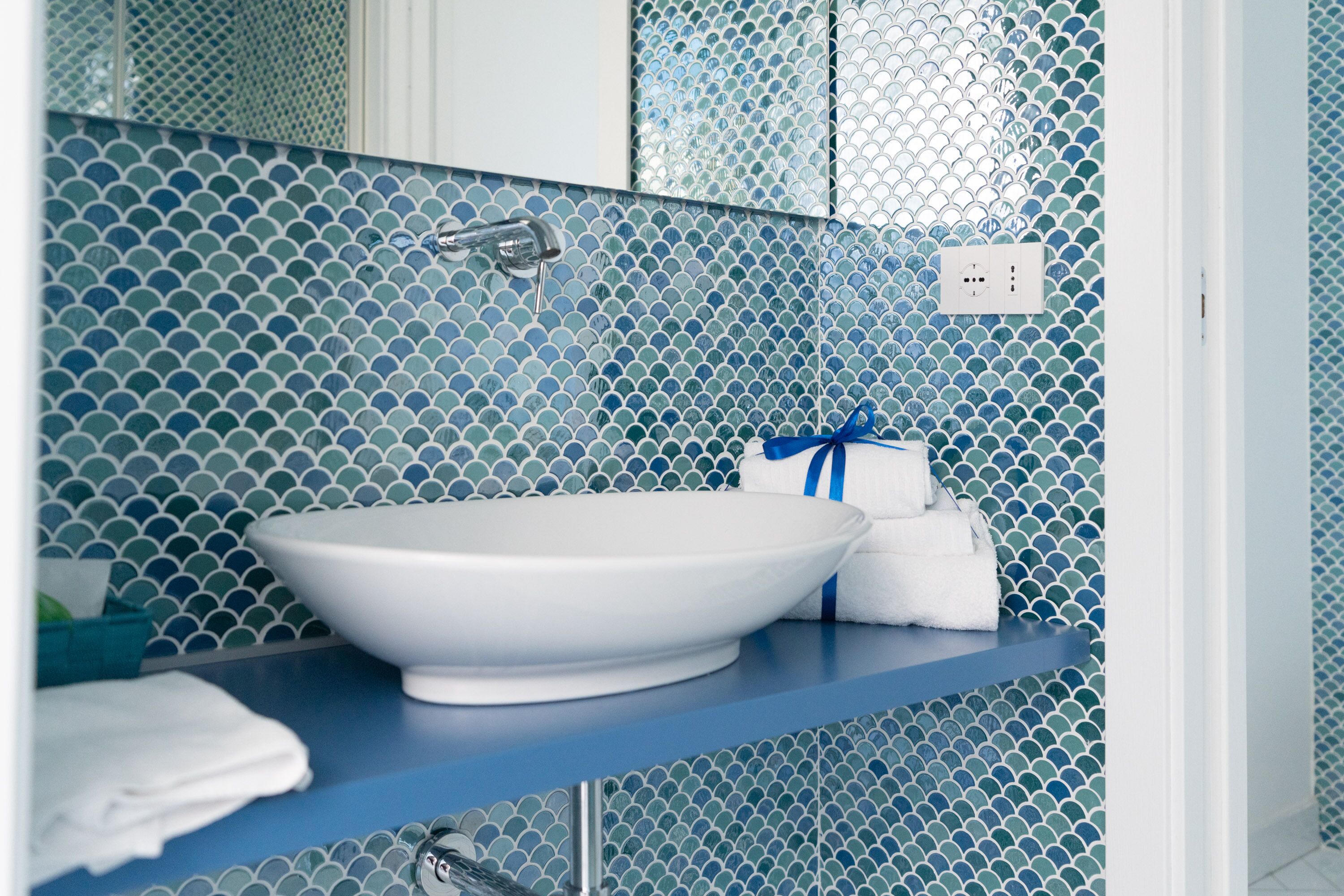 A bathroom with a white sink, blue tiled walls, and a towel rack with towels.