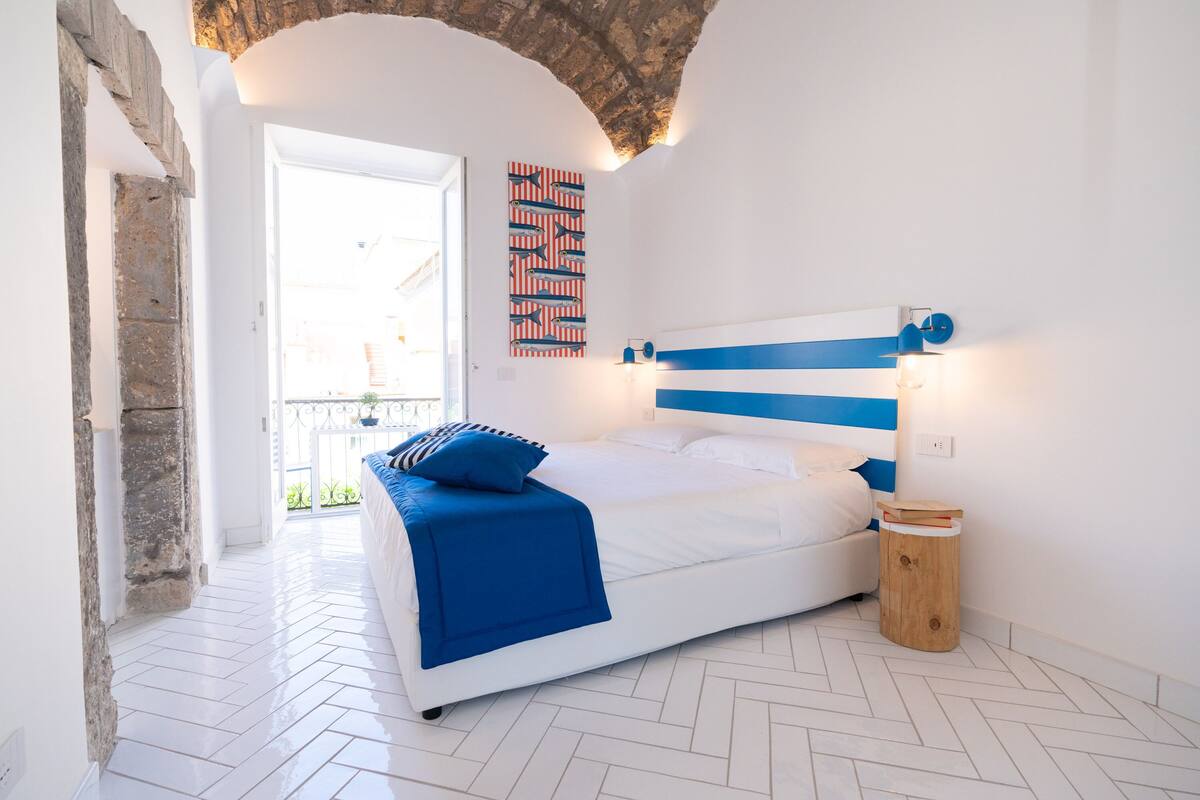 A bedroom with a white bed, blue and white striped headboard, a blue throw blanket, and a wooden nightstand.