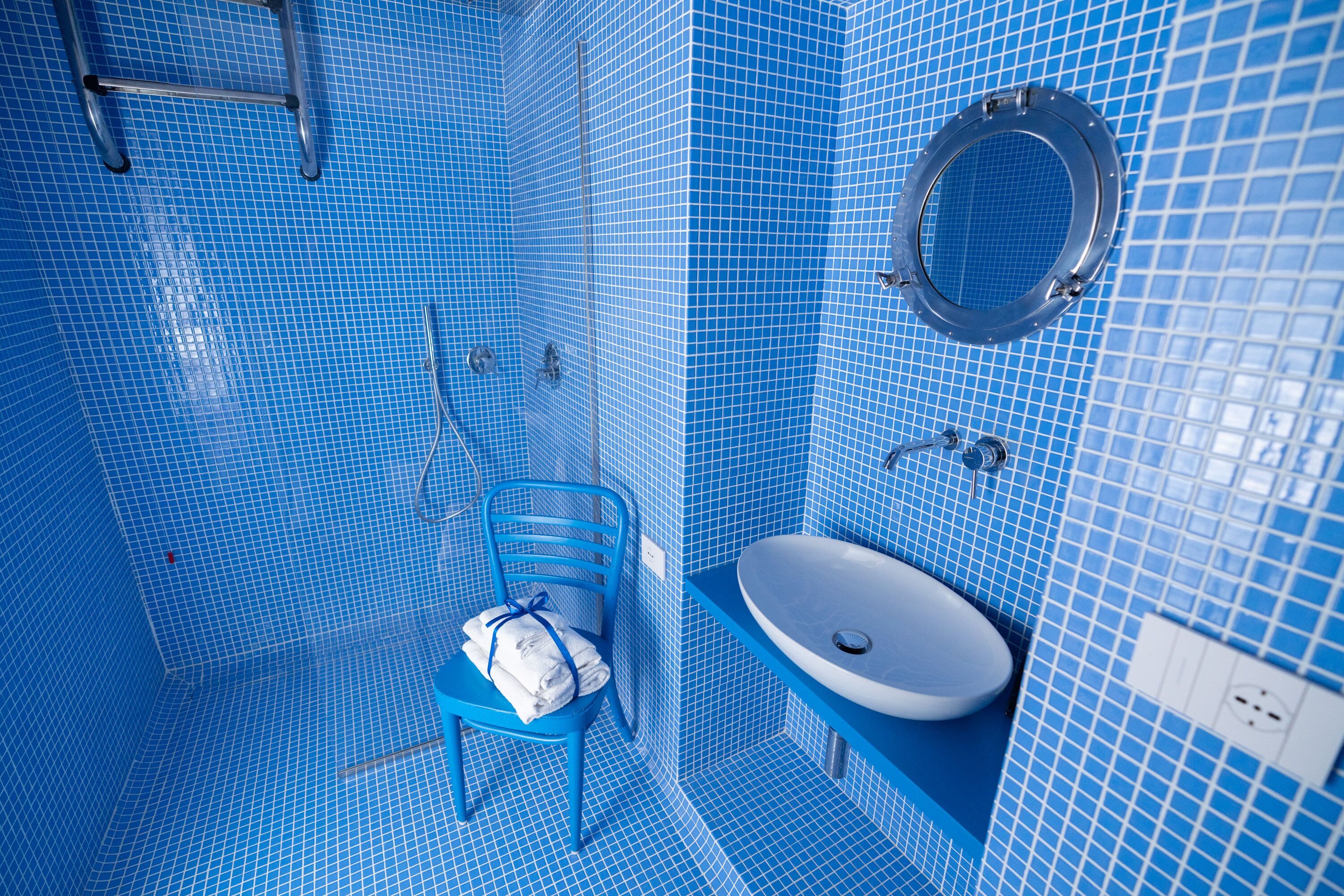 A bathroom with blue tiled walls, a white sink, and a blue chair with towels.