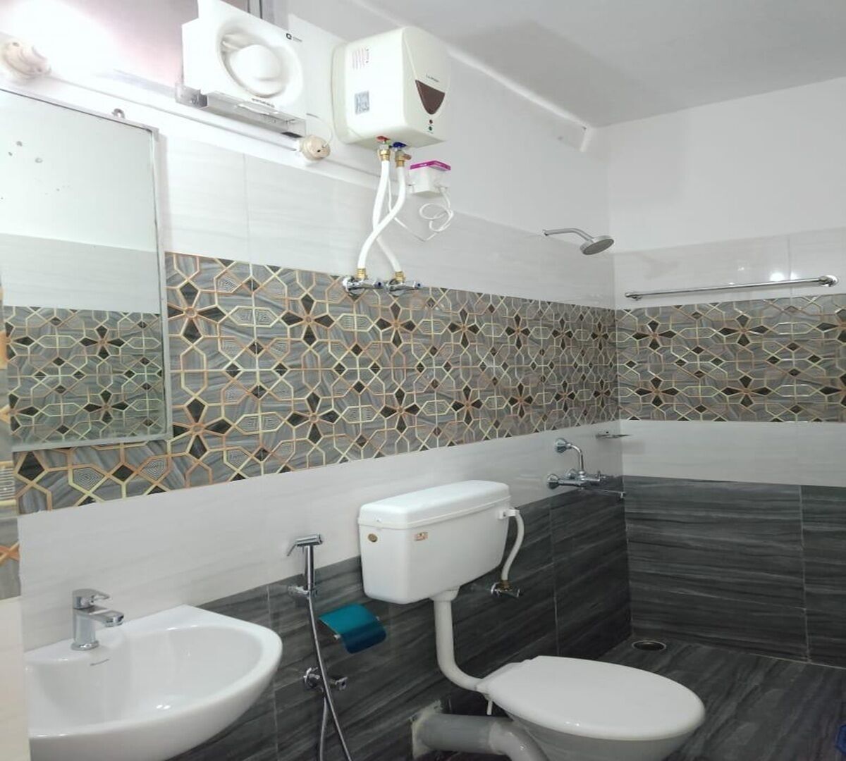 A modern bathroom with a toilet, bidet, and sink, featuring geometric patterned tiles and a white toilet tank.