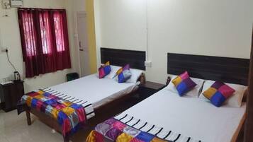 A hotel room with two single beds, each with a colorful quilt, a wooden headboard, and a white wall.