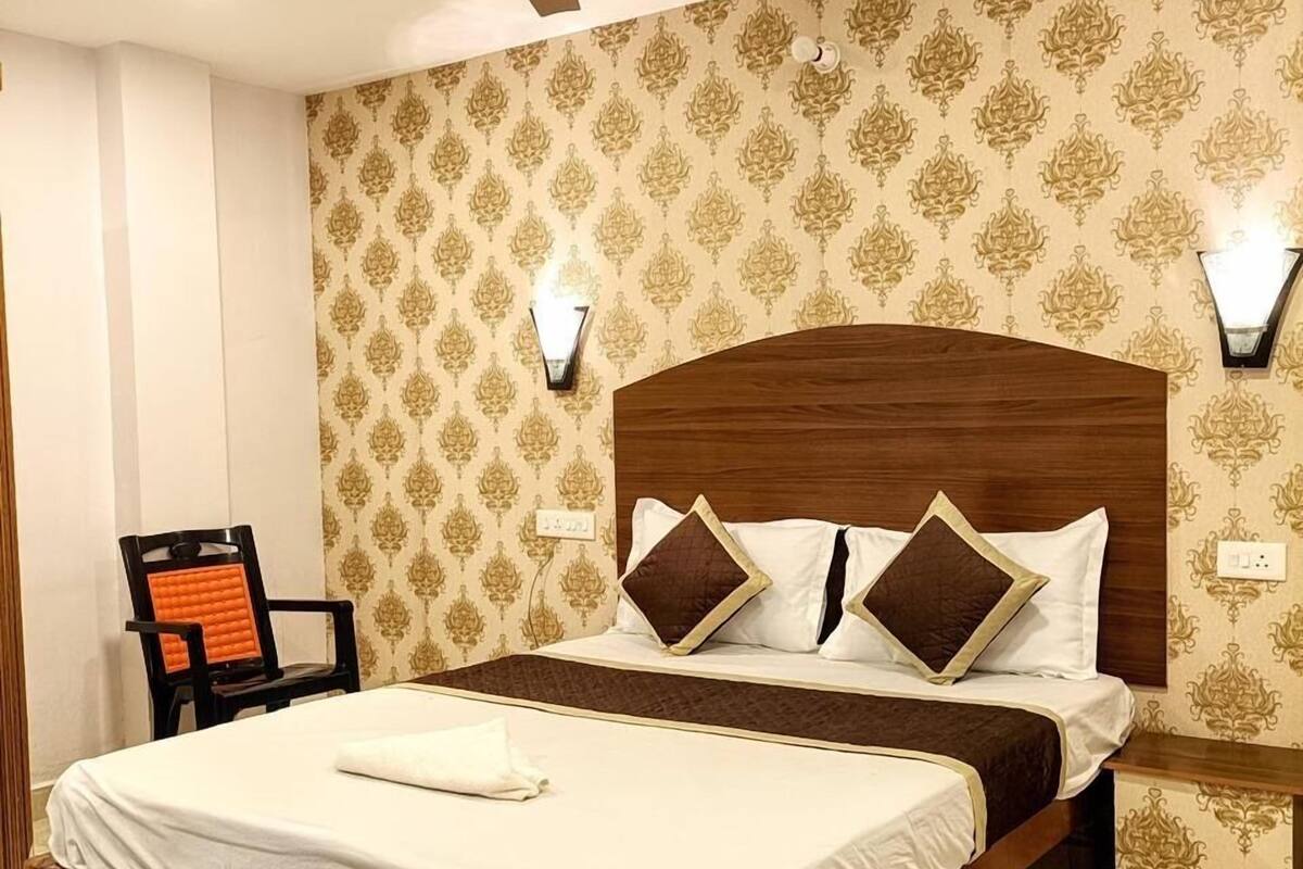 Cama bem arrumada com cabeceira de madeira, ventilador de teto, papel de parede estampado e mesa de cabeceira com luminária.