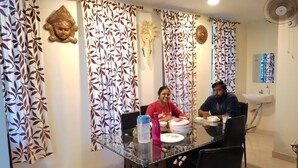 A dining area with a glass table, chairs, and decorative curtains with leaf patterns. - Aashrey Bed and Breakfast (Port Blair)
