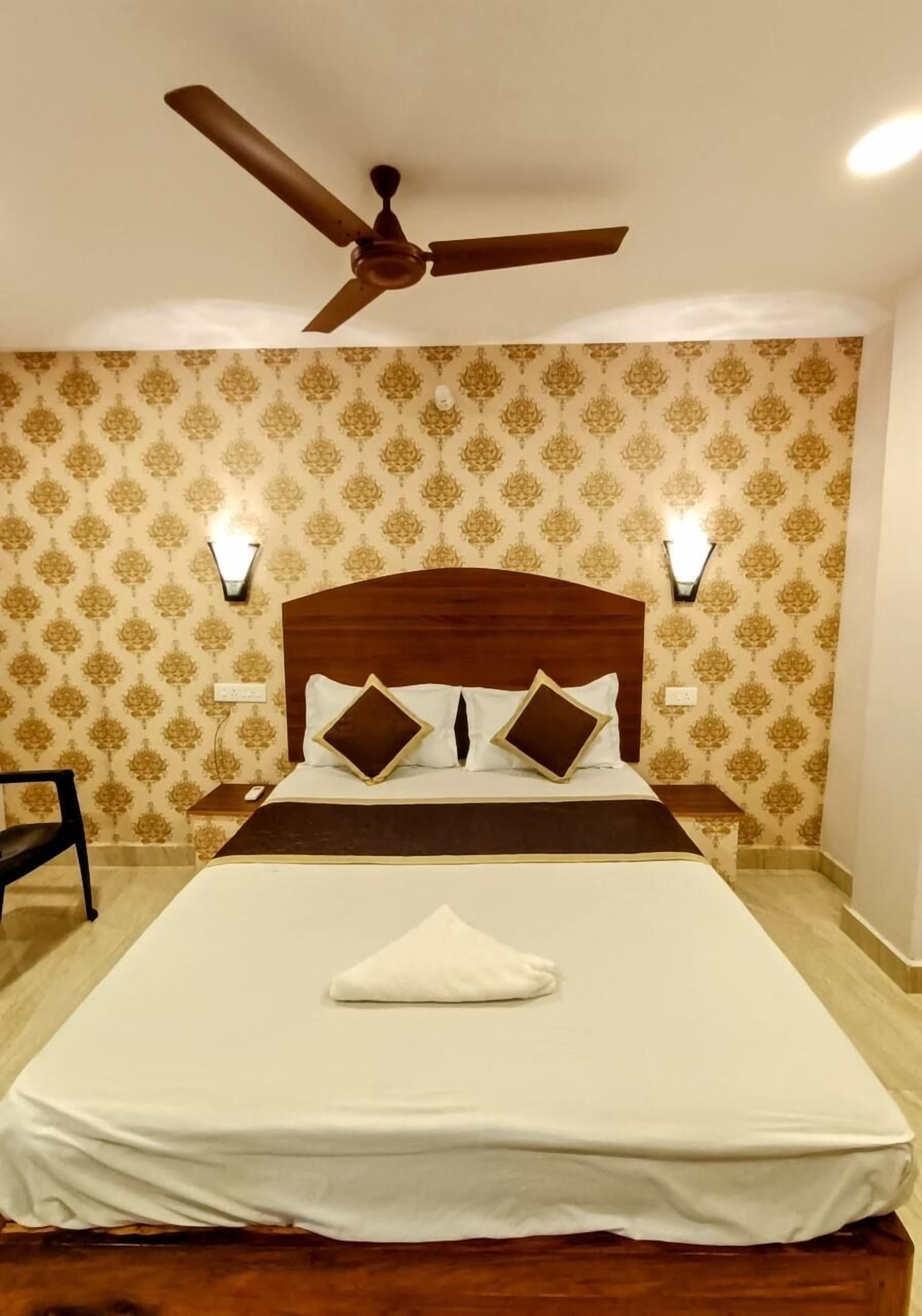 Habitació d'hotel amb un llit gran, amb capçalera de fusta, dues làmpades fixes a la paret, un ventilador de sostre i paper pintat amb motius.