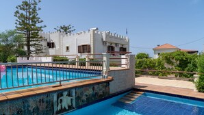 A swimming pool with a stone mosaic border, a castle-like building in the background, and a clear blue sky. - villa Gregory (Chania)