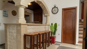 A bar area with a stone counter, wooden stools, a potted plant, a clock, and a wooden door. - villa Gregory (Chania)