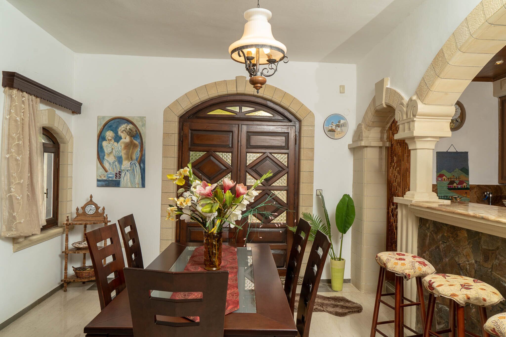 A dining area with a wooden table, chairs, a vase of flowers, and a hanging light fixture.